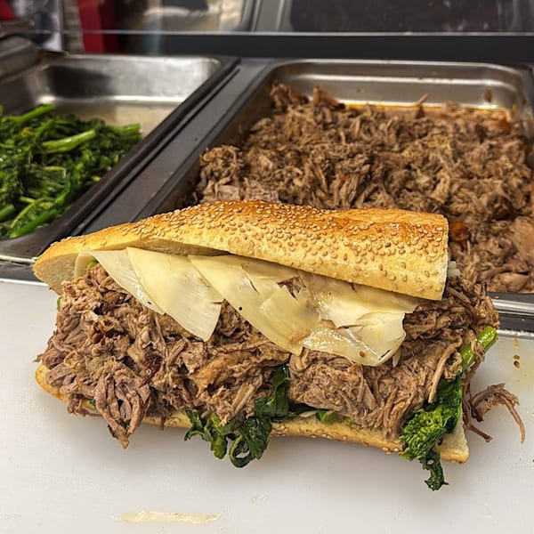 A Gabagool Italian sandwich with shredded meat, cheese, and greens on a sesame seed bun.