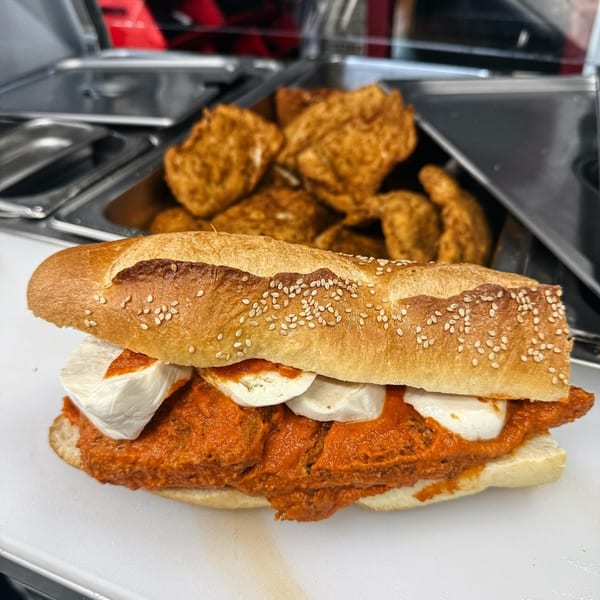 Gabagool's chicken parmesan hero with melted mozzarella and red sauce, with fried chicken in the background.